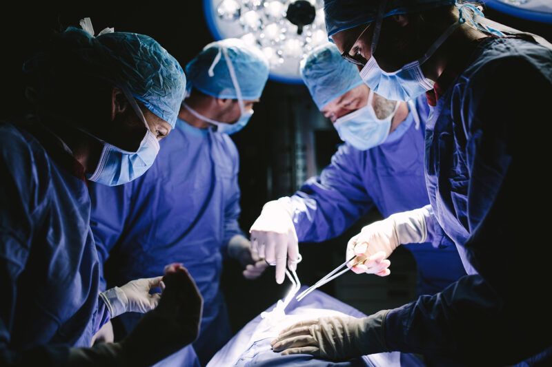 surgeons with gloves and blue scrubs performing surgery